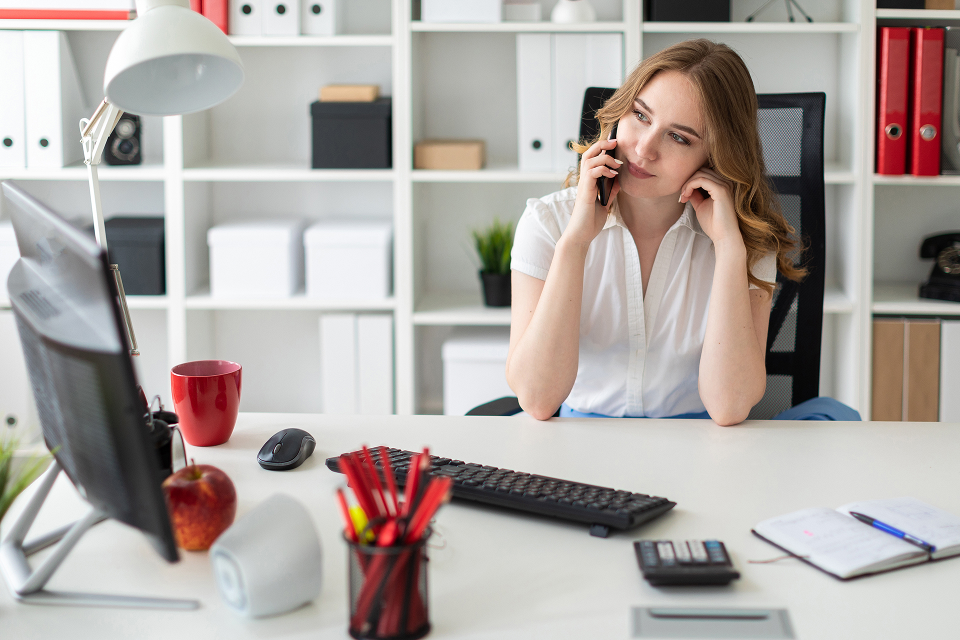 Beautiful young girl is sitting in the office and talking on the phone. Beautiful young girl is sitting in the office and talking on the phone.